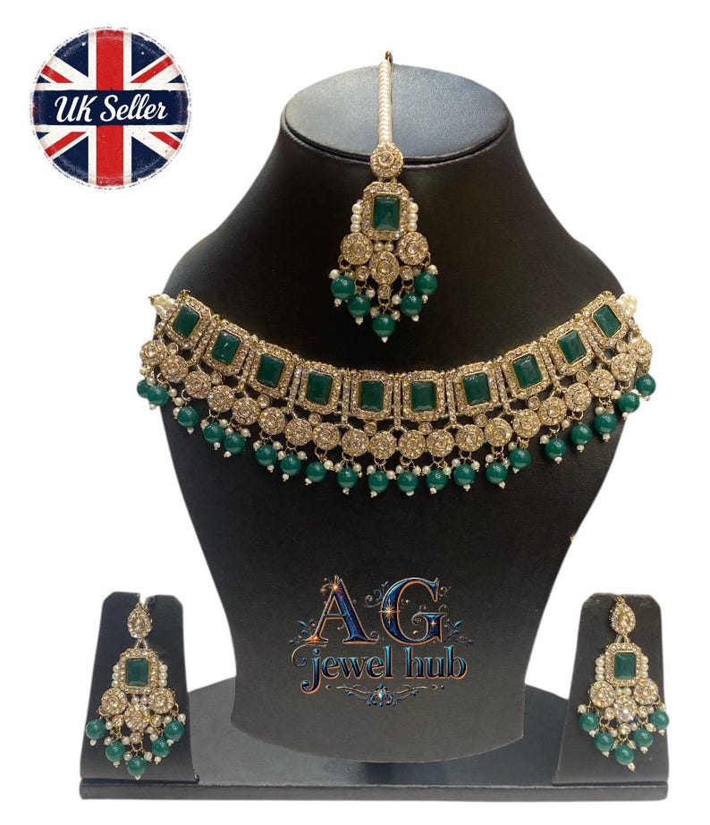 May include: A gold-toned jewelry set featuring emerald green square-cut stones and small green bead accents. The set includes a necklace, earrings, and a headpiece, all displayed on a black mannequin. The text "AG Jewel Hub" is visible.
