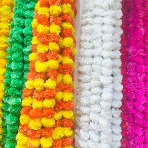 Puede incluir: Una colección de guirnaldas coloridas hechas de flores artificiales. Las guirnaldas son de varios colores, incluyendo amarillo, verde, naranja, blanco y rosa. Las flores están densamente empaquetadas, creando una apariencia completa y texturizada. Estas guirnaldas probablemente se utilizan para la decoración.