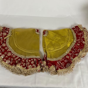 May include: Two fan-shaped garments, likely part of a set. The upper section is a golden yellow, with a deep red lower edge featuring gold sequin and floral embroidery. Gold fringe trims the edges, giving a luxurious feel.