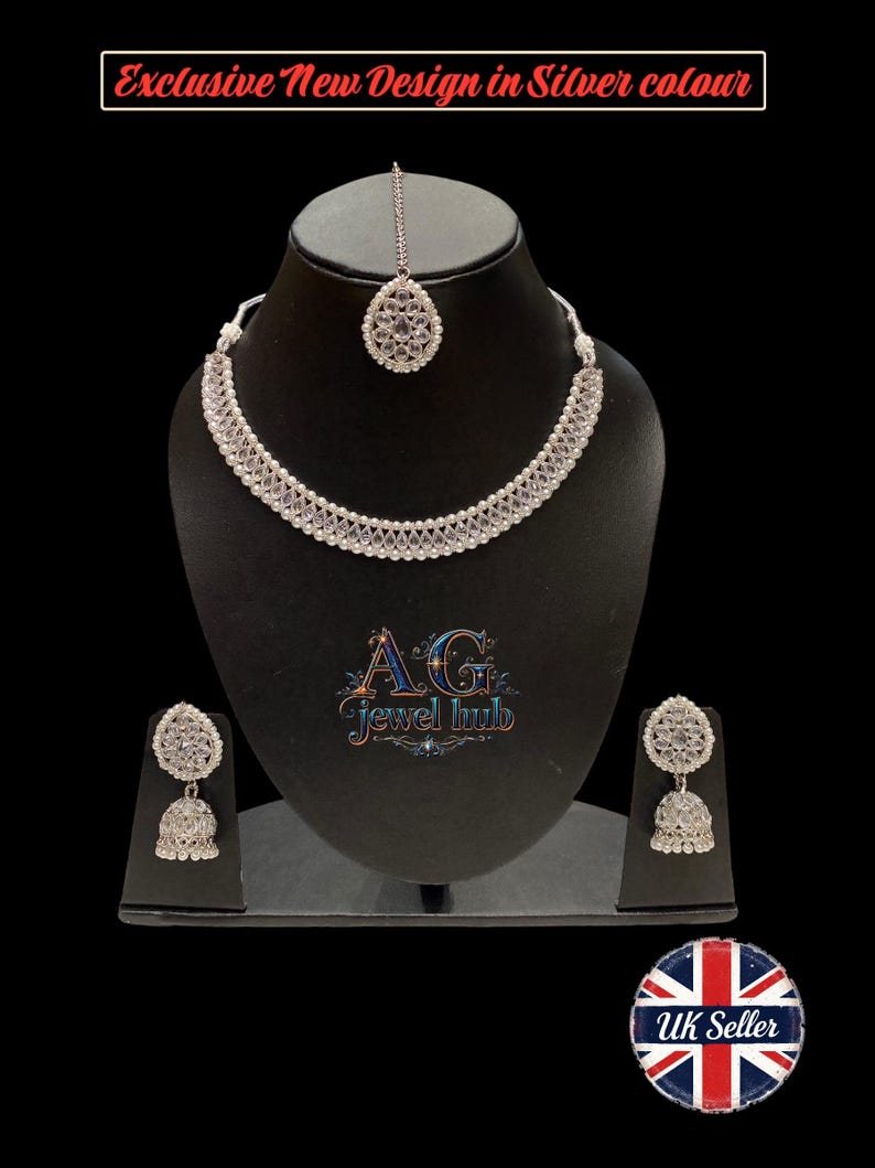 K&ouml;nnte beinhalten: Ein silberfarbenes Schmuckset, bestehend aus Halskette, Ohrringen und Kopfschmuck, pr&auml;sentiert auf einer schwarzen B&uuml;ste. Die Halskette und die Ohrringe weisen detaillierte Designs auf. Der Text "Exclusive New Design in Silver colour" ist sichtbar.