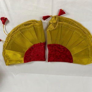 Puede incluir: Dos abanicos decorativos, cada uno con forma semicircular. Los abanicos son principalmente dorados con una base roja texturizada en forma de semicírculo. Cada abanico tiene una borla roja y un acento floral rojo.