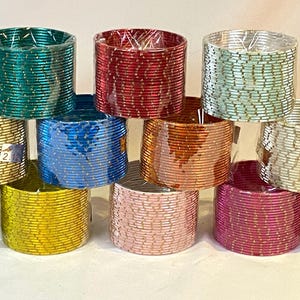 以下が含まれることがあります： 緑、金、青、赤、ピンクなど、さまざまな色合いのカラフルなバングルのコレクション。 バングルはピラミッド型に積み重ねられており、鮮やかな色と質感が示されています。 各バングルは透明なプラスチックで包まれています。