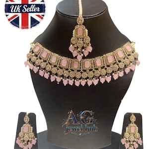 May include: A gold-toned jewelry set featuring a necklace, earrings, and a headpiece. The set includes pink square-shaped stones and small pink bead accents. The jewelry is displayed on a black mannequin head and stand. The text "AG Jewel hub" is visible.
