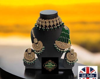 May include: A gold-coloured jewellery set with green and white beads, comprising a choker, earrings, and a headpiece, presented on a black display stand. The set showcases detailed patterns and beadwork, suitable for formal events.