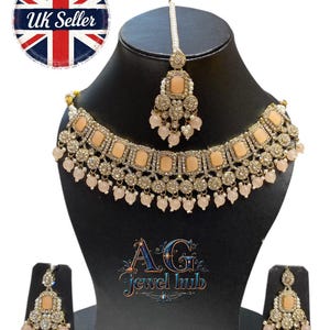 May include: A peach-colored and silver-toned jewelry set, including a necklace, earrings, and a headpiece, displayed on a black mannequin. The necklace and earrings feature square peach-colored stones and dangling beads. The set is labeled "UK Seller".