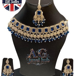 May include: A gold-toned jewelry set featuring a necklace, earrings, and a headpiece, all adorned with square blue gemstones and small blue beads. The set is displayed on a black mannequin. The text "AG jewel hub" is visible.