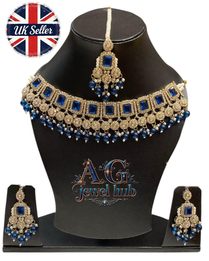 May include: A gold-toned jewelry set featuring a necklace, earrings, and a headpiece, all adorned with square blue gemstones and small blue beads. The set is displayed on a black mannequin. The text "AG jewel hub" is visible.