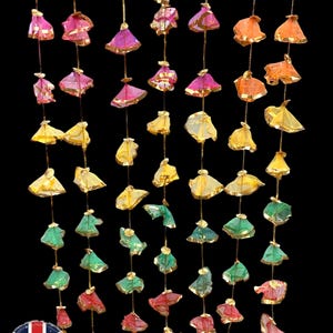 Puede incluir: Una guirnalda decorativa con múltiples adornos pequeños en forma de campana, en varios colores, incluyendo azul, rosa, naranja, amarillo, verde y rojo. Cada adorno tiene un borde dorado y cuelga de un hilo dorado sobre un fondo negro.