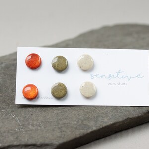 May include: Six small round ceramic earrings in orange, green, and white. The earrings are displayed on a white card with the text "sensitive ears studs".