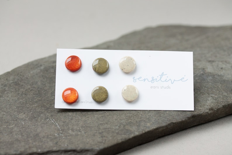May include: Six small round ceramic earrings in orange, green, and white. The earrings are displayed on a white card with the text "sensitive ears studs".