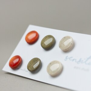 May include: Five ceramic earrings in various colors and patterns. The earrings are displayed on a white card with the text "sensible" written on it.