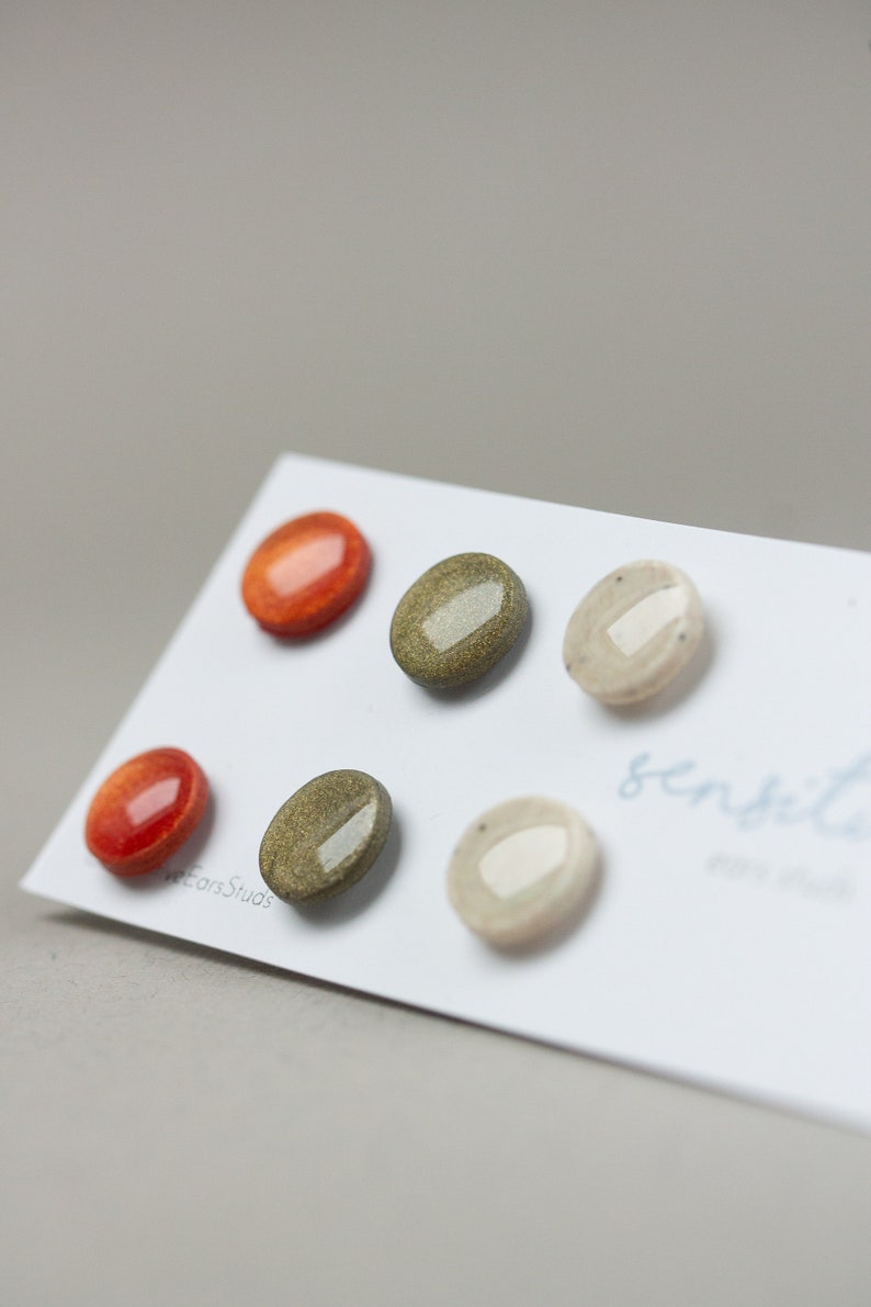 May include: Five ceramic earrings in various colors and patterns. The earrings are displayed on a white card with the text "sensible" written on it.