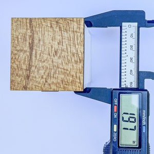 Puede incluir: Un primer plano de un bloque de madera que se mide con un calibre digital. El calibre muestra 1,97 pulgadas.