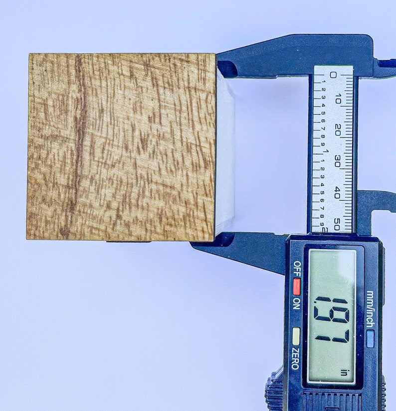 Puede incluir: Un primer plano de un bloque de madera que se mide con un calibre digital. El calibre muestra 1,97 pulgadas.