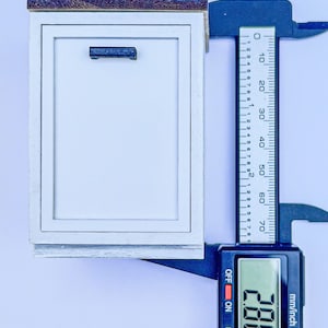 Puede incluir: Un armario blanco con una tapa de madera y una manija azul. Un calibrador digital mide el armario a 7,32 cm.
