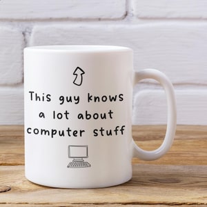 May include: A white ceramic mug featuring a black hand-drawn arrow pointing upwards, the text "This guy knows a lot about computer stuff" in a simple sans-serif font, and a small black line drawing of a desktop computer monitor and keyboard.