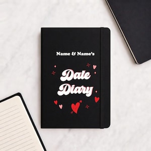 May include: A black Date Diary notebook with the text "Name & Name's" at the top. The words "Date Diary" are in a white, retro font. Red hearts and stars decorate the cover. A black elastic band holds the notebook closed.