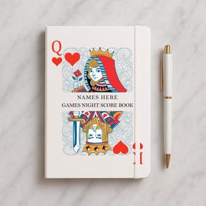 May include: A white notebook featuring a Queen of Hearts playing card design. The notebook has the text "NAMES HERE GAMES NIGHT SCORE BOOK". A white and gold pen is placed beside the notebook.