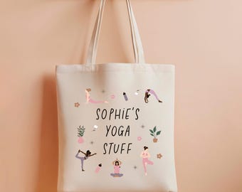 Könnte beinhalten: Cremefarbene Tragetasche mit dem Text "Sophie's Yoga Stuff". Die Tasche zeigt Illustrationen von Yoga-Posen, Pflanzen und kleinen dekorativen Elementen. Sie hängt an einem hölzernen Kleiderhaken.