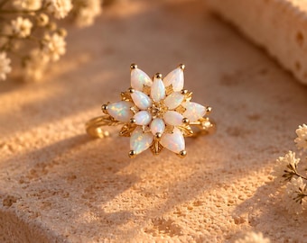 May include: A gold ring featuring a central cluster of marquise-cut opals arranged in a floral star pattern. The iridescent white stones are set in a yellow gold band with delicate leaf-like metal details extending from the base of the petals.