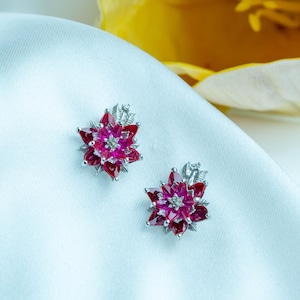 Può includere: Un paio di orecchini a forma di fiore in rubino rosso e diamanti. Gli orecchini sono incastonati in argento e hanno un delicato motivo floreale.