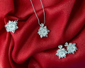 May include: A silver-toned jewelry set consisting of a necklace with a flower-shaped pendant, a matching ring, and a pair of stud earrings. Each piece features a cluster of clear, marquise-cut stones arranged to resemble a blooming flower.