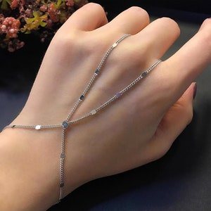 Könnte beinhalten: Ein silbernes Kettenarmband mit kleinen, runden, flachen Anhängern. Das Armband ist so konzipiert, dass es am Handgelenk getragen wird und den Arm hinaufreicht, wobei die Kette bis zu den Fingern reicht.
