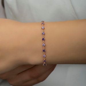 May include: A delicate rose gold bracelet with a chain of small round purple gemstones.