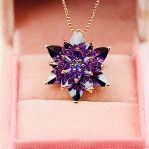 May include: A pendant necklace featuring a multi-layered flower design with deep purple, faceted marquise-cut stones set in a rose gold-toned metal frame, suspended from a delicate matching rose gold-toned beaded chain.
