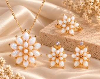 May include: A gold-toned jewelry set consisting of a necklace, a ring, and a pair of stud earrings. Each piece features a floral design composed of marquise-cut, iridescent white opal-like stones arranged in layers around a central point.