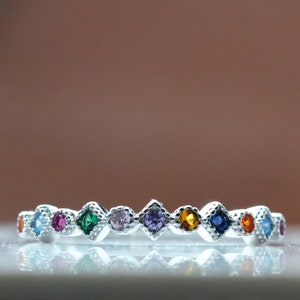 May include: A silver band ring with a row of colorful square-shaped gemstones. The gemstones are set in a silver band and are arranged in a rainbow pattern.