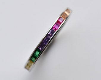 Puede incluir: Un anillo de banda de plata con una banda de piedras preciosas cuadradas de colores arcoíris.
