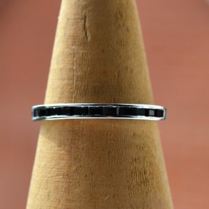 May include: A silver band ring with a row of black square-shaped stones.