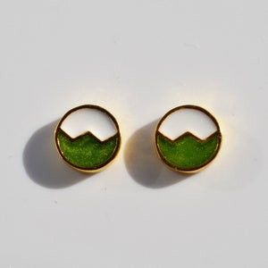 May include: A pair of small, round earrings with a white and green enamel design. The earrings are gold-toned and have a simple, geometric shape.