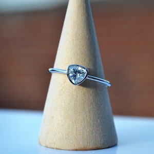 May include: A silver ring with a triangular shaped clear gemstone set in a bezel setting.