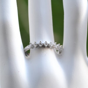 Könnte beinhalten: Ein silberner Bandring mit einer Reihe kleiner, klarer Zirkonia-Steine, die in einer geschwungenen Linie eingefasst sind.