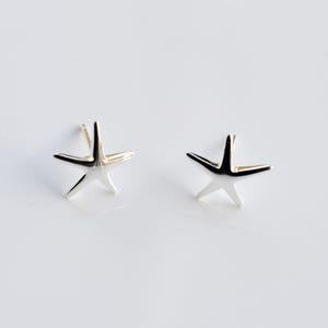 May include: A pair of polished silver-toned starfish stud earrings. Each earring features a five-pointed star design with smooth, reflective surfaces and a post backing, presented as a matching set of two individual pieces for ear adornment.