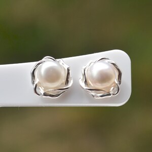 Può includere: Un paio di orecchini d'argento con un perla in ogni orecchino. Le perle sono bianche e rotonde, e gli orecchini hanno la forma di un fiore.