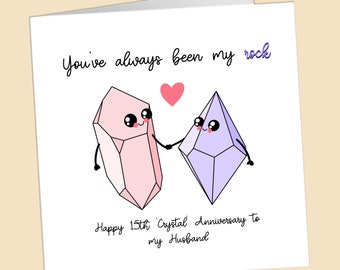 May include: A greeting card featuring a pink and purple crystal illustration. The card reads "You've always been my rock" and "Happy 15th Crystal Anniversary to my Husband".
