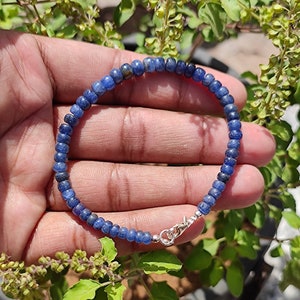 May include: A blue gemstone beaded bracelet with a silver clasp. The bracelet is made of small, round beads and is approximately 7 inches in length.