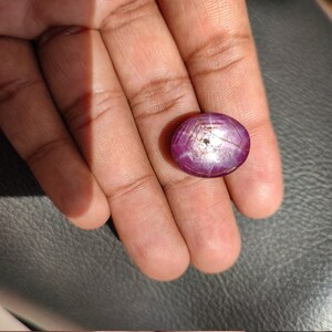 May include: A round, cabochon-cut, pink ruby gemstone with a star-like pattern in the center. The stone is set in a silver ring.