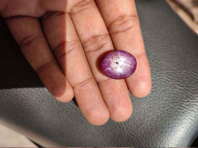 May include: A round, cabochon-cut, pink ruby gemstone with a star-like pattern in the center. The stone is set in a silver ring.