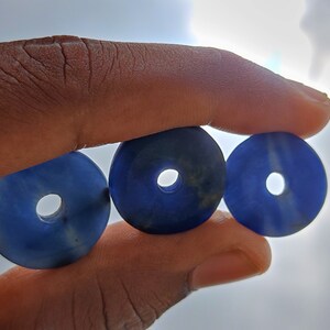 以下が含まれることがあります： 中央に穴の開いたドーナツ型の青いビーズが3つ。ビーズは滑らかで磨かれた素材で作られています。