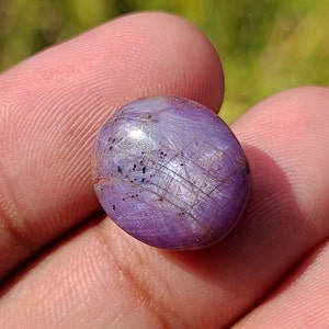 May include: A purple gemstone with a cabochon cut and a silvery sheen. The stone has a striated pattern and is set in a silver ring.