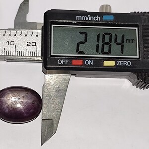 May include: A close-up of a purple gemstone being measured with a digital caliper. The caliper reads 2.184 mm.