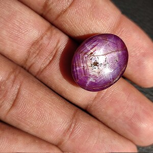 May include: A deep purple oval-shaped gemstone with a star-like pattern and a silver sheen. The gemstone is set in a silver ring.