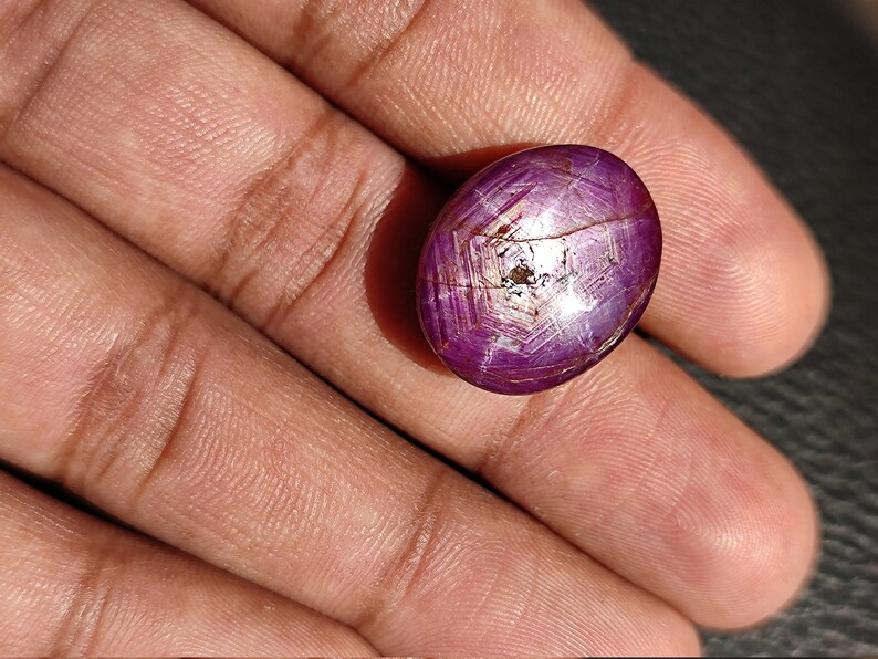 May include: A deep purple oval-shaped gemstone with a star-like pattern and a silver sheen. The gemstone is set in a silver ring.