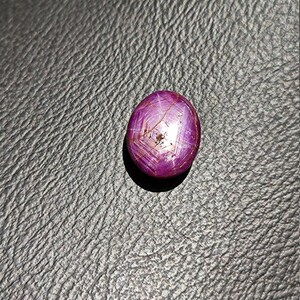 May include: A deep pink oval-shaped gemstone with a star-like pattern and red inclusions.