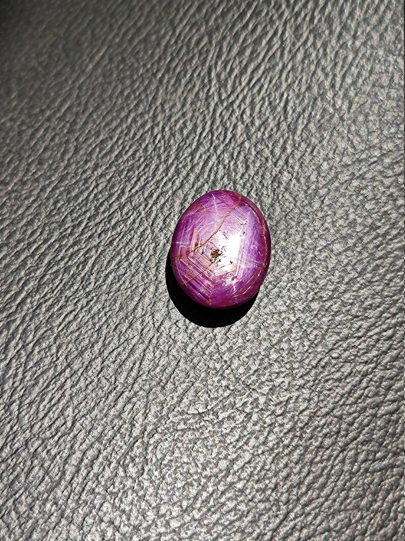 May include: A deep pink oval-shaped gemstone with a star-like pattern and red inclusions.