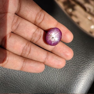 May include: A pink oval-shaped gemstone with a star-like pattern inside. The gemstone is set in a silver ring.